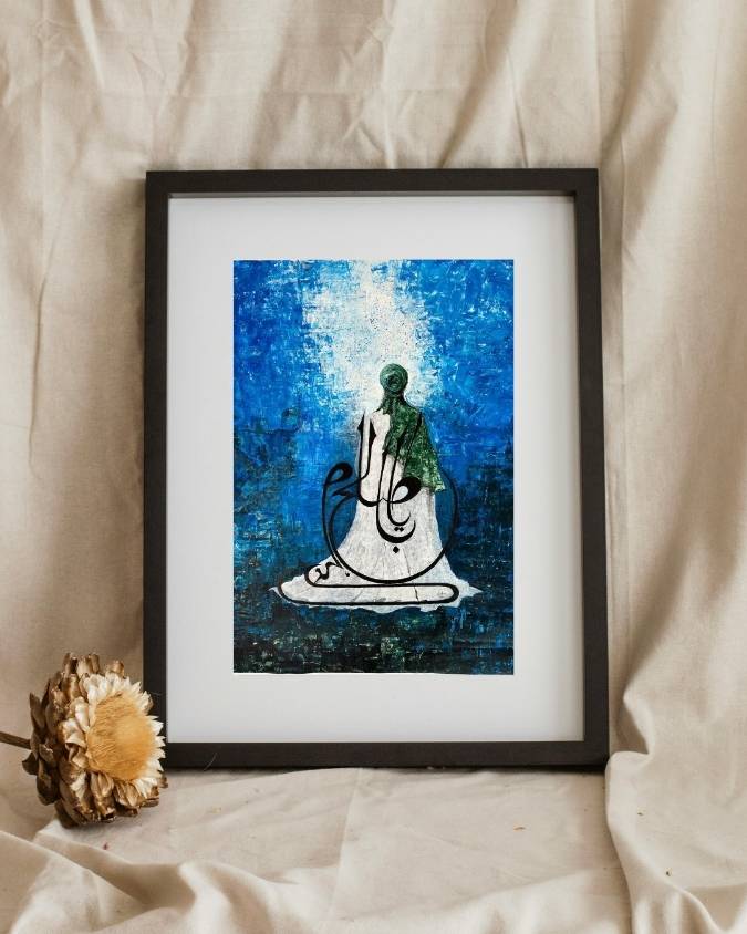 Al-Faraj artwork framed on cream fabric beside a dried flower, seated figure in green robes on radiant blue